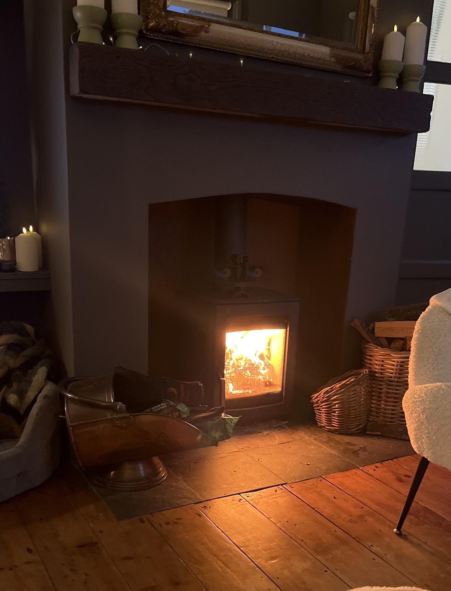 A lit woodburner fitted in a fireplace recess on a slate hearth, with candles on the mantel